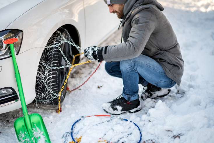 Homme qui installe des chaînes sur ses pneus neige